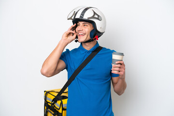Young caucasian man with thermal backpack isolated on white background holding coffee to take away and a mobile