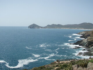 Mar con espuma en primer plano y rocas de borde de costa y al fondo  horizonte con colinas y...