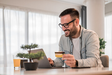 Cheerful businessman making online payment while using laptop at office desk