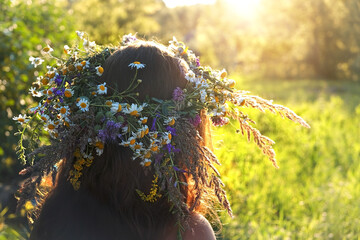 Girl in flower wreath rear view , close up, sunny green natural blurred background. Floral crown, symbol of summer solstice. Slavic ceremony on Midsummer, wiccan Litha sabbat. summer season concept. - obrazy, fototapety, plakaty