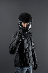 Studio shot of Motorcyclist biker in black equipment points and looks at camera.
