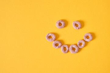 colored breakfast cereals laid out in the shape of a smiley face on a yellow background top view