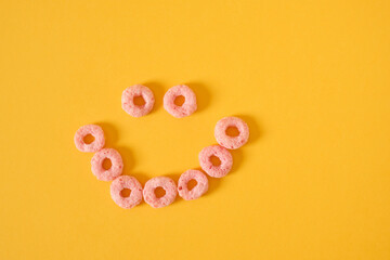 colored breakfast cereals laid out in the shape of a smiley face on a yellow background top view