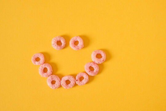 colored breakfast cereals laid out in the shape of a smiley face on a yellow background top view - Powered by Adobe
