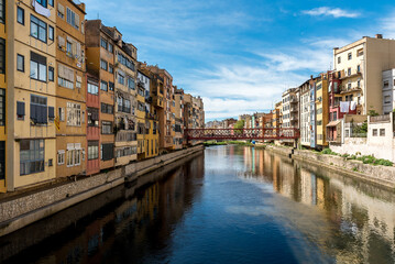 Fototapeta na wymiar Colorful yellow and orange houses reflected in water river Onyar, in Girona, Catalonia, Spain. Church of Sant Feliu and Saint Mary Cathedral at background.