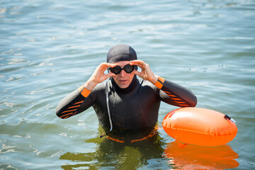 athlete swimmer in a wetsuit with a buoy, puts on goggles in the water