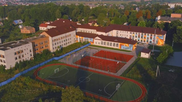Exterior of school building with playground. Ground in the park. School and playground landscape. Basketball court new fenced in park. Trees urban place for children.