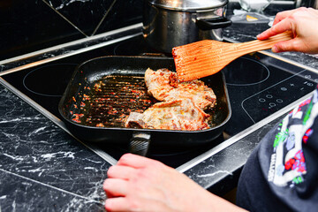 Fried pork steaks in a frying pan. A woman turns meat for frying.