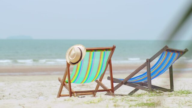 Colorful beach chairs with hat on the beach and sea waves and blue sky in the background.