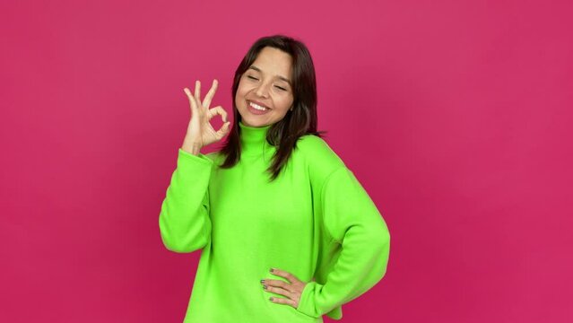 Young brunette woman showing ok sign with fingers over isolated background