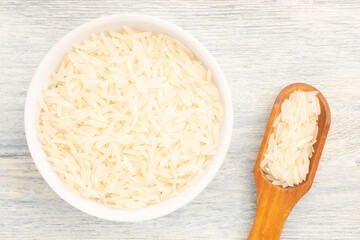 Long Basmati rice in ceramic bowl and wooden scoop on white wooden background. Macro. Flat lay. Vegetarian food concept