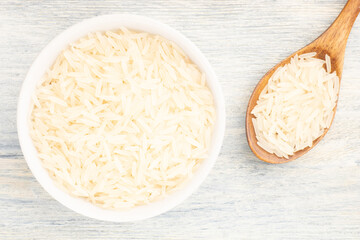 Long Basmati rice in ceramic bowl and wooden spoon on white wooden background. Macro. Flat lay. Healthy food concept