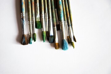 Fototapeta premium old worn brushes on white paper are folded in a row for drawing, a blank for a designer