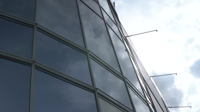 Office glass urban, business building exterior pan and tilt, revealing sky and sun in a cloudy day. Slow motion dutch angle panorama.