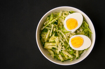 diet cabbage salad with cucumber and boiled egg on a black background, top view, a place to copy