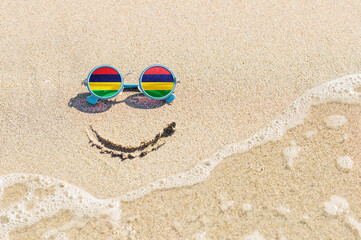 A painted smile on the beach and sunglasses with the flag of Mauritius. The concept of a positive and successful holiday in the resort of Mauritius.