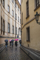 group of people holding colourful umbrellas walking along narrow street, Old Town, Prague, Czech Republik