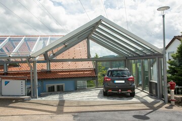 Moderner Carport mit Glasdach und Stahlträgerkonstruktion im Einfahrtsbereich eines Wohnhauses