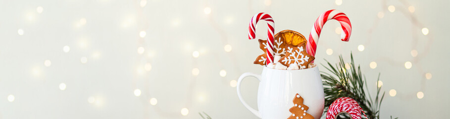 Hot winter drink in a white mug: cozy home composition with homemade gingerbread cookies, candy...