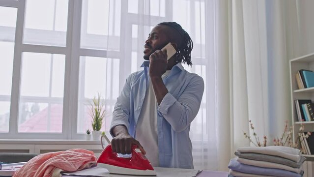 Excited man talking on phone, oblivious of iron on clothes, irresponsibility