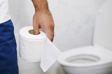 Man suffers from diarrhea hand hold tissue paper roll in front of toilet bowl. constipation in...