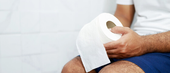 Man suffers from diarrhea hand hold tissue paper roll in front of toilet bowl. constipation in...