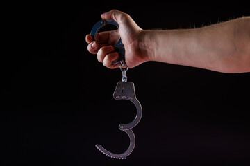 bare caucasian hand holding opened silver steel handcuffs on black background.