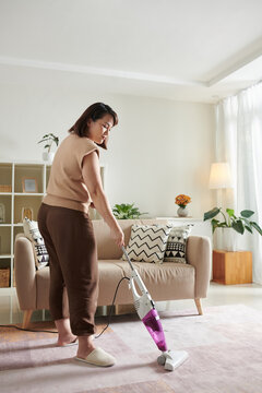 Woman in comfy homewear vacuum cleaning carpet in living room on Saturday morning