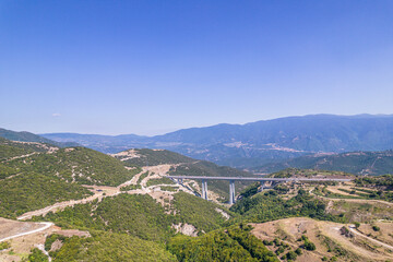 Fototapeta na wymiar Panoramic view of top of mountains, highway bridge in sunny summer weather in Greece. Aerial view