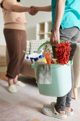 Cleaning service worker with bucket of detergents and tools shaking hand of client after finishing...