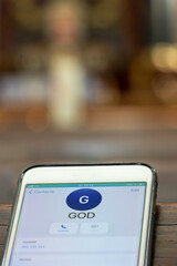 Calling God with a mobile phone on the table of a prayer bench in the church, close up.