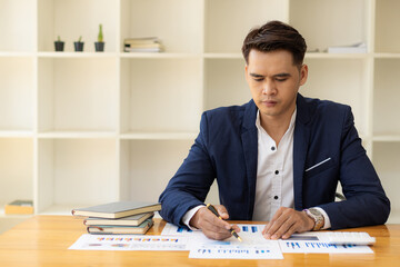 Asian male businessman with documents and laptop computer doing accounting and analytics work. data charts and graphs and use a calculator to calculate numbers Business Finance and Accounting Concepts