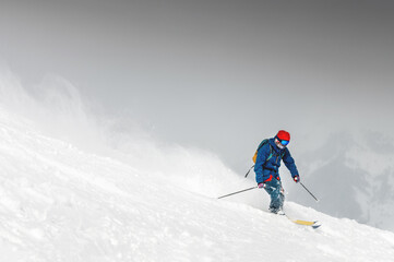 Fototapeta na wymiar Skiing, skier, frisky - freeride, a man is stylishly skiing on a snowy slope with snow dust plume behind him
