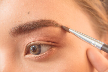 Closeup of a MUA or Makeup artist using brow filler on a slanted eyeliner brush to shape the...