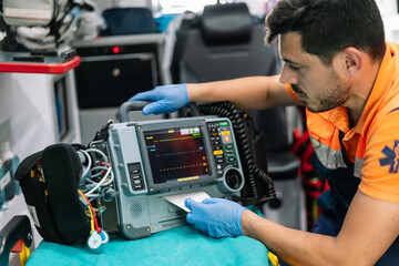 portrait of a handsome young paramedic working with a defibrillator monitor inside an ambulance.