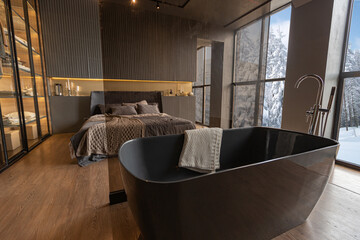 a bedroom and a free-standing bath in a chic expensive interior of a luxurious country house with huge panoramic windows and a magnificent view of the divine forest
