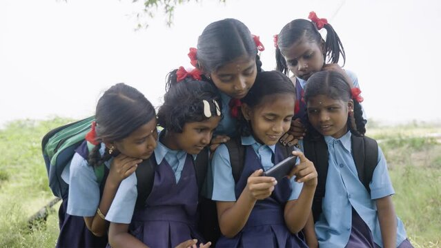 school girl kid playing video game on mobile phone while group of kids surrounded - concept of technology addiction, entertainment and togetherness.
