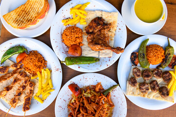 Top view of table scene with assorted take out or delivery foods. Meat and chicken doner kebab sandwich, wrap and on the plate with vegetables and sauce, including fries and pickles.