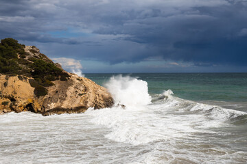 Stormy coastline with water splash and dark sky, sandy beach with turquoise sea, Sitges, Spain