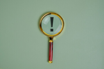 Exclamation mark under magnifying glass, on green background.