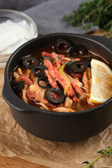 Solyanka soup with meat, sausage, vegetables, olives and lemon in bowl