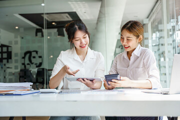 Two Asian business women work together to end work and taxes at the office.