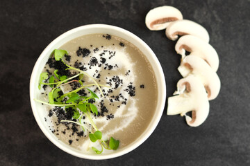 French cuisine hot food delivery - mushrooms soup closeup in eco paper bowl on black background. Delivery healthy eating concept.
