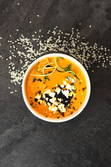 Carrot soup with feta cheese and microgreens in a round black eco container on a dark background. Healthy food delivery concept.	
