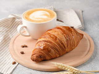 Large croissant and a cup of cappuccino on a light background