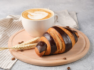 Large croissant and a cup of cappuccino on a light background