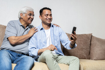 Happy old father and son using phone together, and having fun