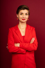 A boss business woman in bright makeup, a red jacket, a red T-shirt, with bright red lipstick and green shadows, stands on a red background with her arms crossed on her chest. Studio shooting