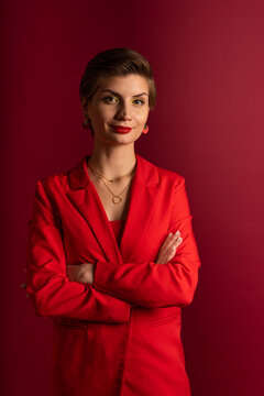 A boss business woman in bright makeup, a red jacket, a red T-shirt, with bright red lipstick and green shadows, stands on a red background with her arms crossed on her chest. Studio shooting