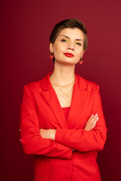 A boss business woman in bright makeup, a red jacket, a red T-shirt, with bright red lipstick and green shadows, stands on a red background with her arms crossed on her chest. Studio shooting